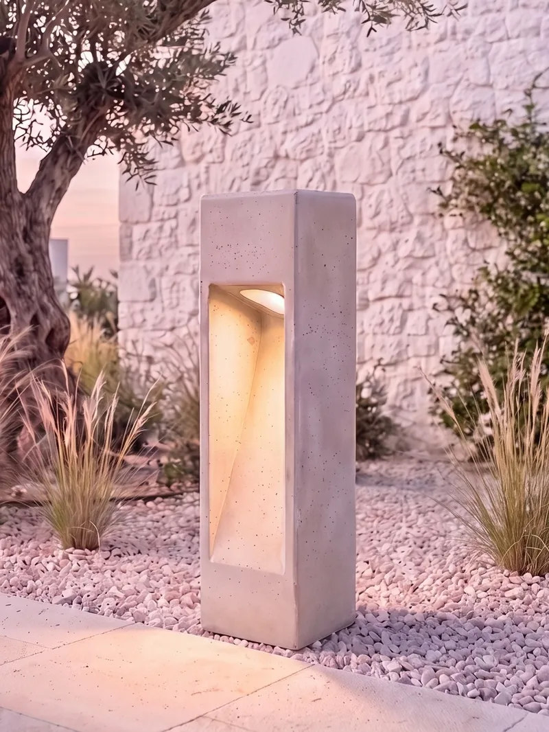 NICHE concrete bollard glowing at dusk in front of an olive tree